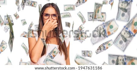 Young hispanic woman wearing casual clothes and glasses smelling something stinky and disgusting, intolerable smell, holding breath with fingers on nose. bad smell