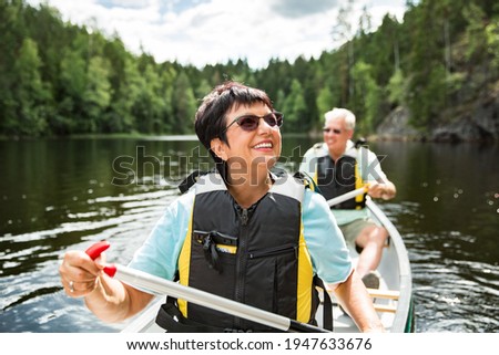Happy mature couple in life vests canoeing in forest lake. Sunny summer day. Tourists traveling in Finland, having adventure.  Royalty-Free Stock Photo #1947633676