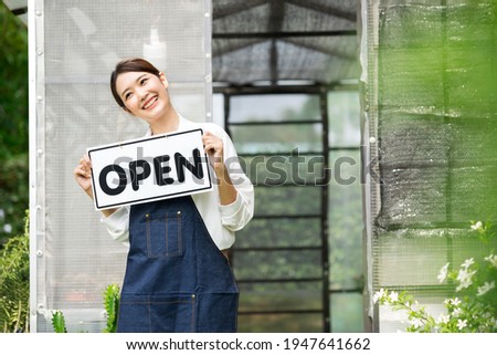 The owner of the tree shop holds a open sign after a long time closed. Cute asian gardener small business open her shop selling small tree for decoration in greenhouse.