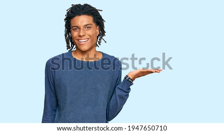 Young african american man wearing casual winter sweater smiling cheerful presenting and pointing with palm of hand looking at the camera. 