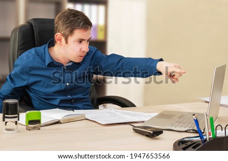 A serious boss at his desk points his index finger at a laptop screen. Office worker. Department manager. Online conference