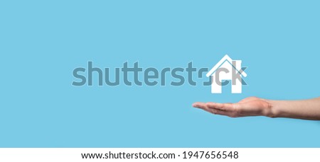 Male hand holding house icon on blue background. Property insurance and security concept.Real estate concept