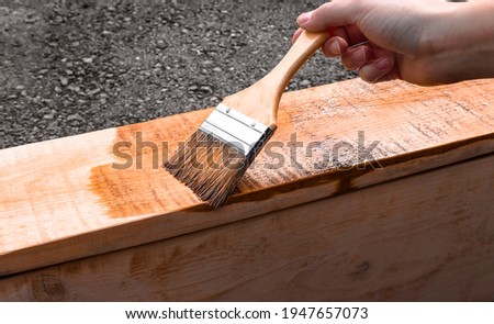 The girl painter makes painting works of wood products with brown paint. DIY, carpenter's work, wood covering protection. Royalty-Free Stock Photo #1947657073