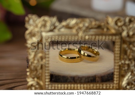 Two golden wedding rings close up with wooden picture frame on wooden background. Wedding invitation card concept. 