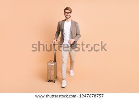 Full size photo of attractive cheerful young man go hold suitcase isolated on pastel beige color background