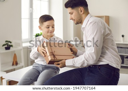Young man getting birthday gift and thanking his little son for surprise. Child giving present box to his dad and wishing him Happy Father's Day. Exchanging presents on special family occasion concept