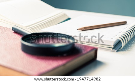 Closeup pencil on notebook with part of opened book and magnifying glass, reading for writing, summarize the content Royalty-Free Stock Photo #1947714982