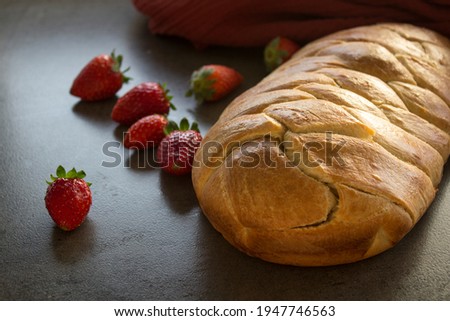 Sourdough challah bread on a table with strawberries. Gray textured background. Homemade loaf close up photo. 