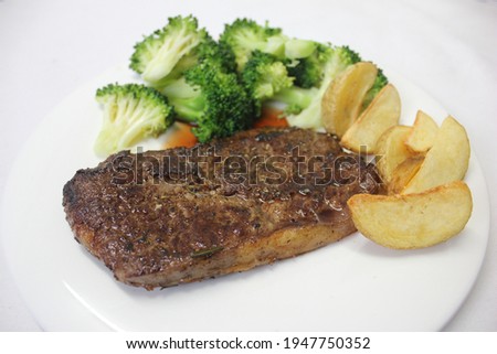 Homemade Delicious Grilled Beef juicy medium rare steak with French fries and boil simmer vegetables(Broccolis) served on clean ceramic white plate on wooden table with tablecloth. Copy space for text