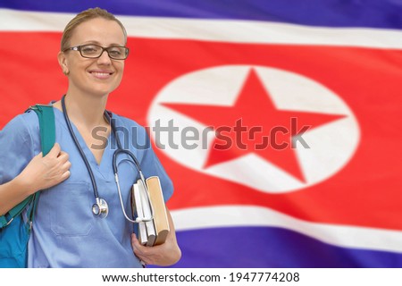Female student doctor with stethoscope and books in hand on the North Korea flag background. Medical education concept. Medical learning in North Korea