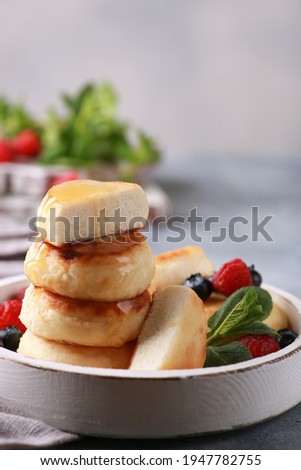 Healthy breakfast. Cheesecakes, cottage cheese pancakes with honey, fresh berries, mint on a white wooden plate on a gray table. Background image, copy space, vertical