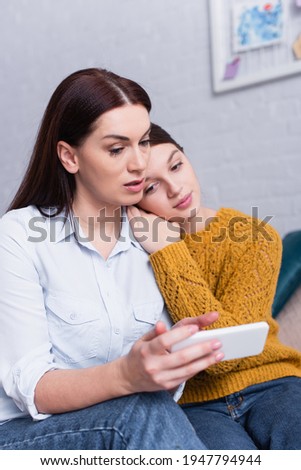 teenage daughter and mother looking at smartphone in bedroom