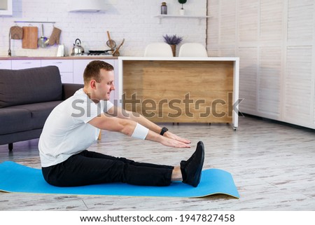 Muscular athletic man in a t-shirt doing warm-up exercises at home. Doing sports at home during the quarantine period. Fitness outside the gym