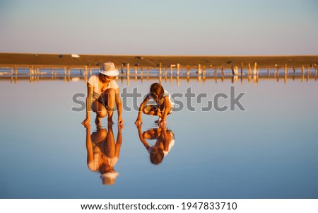 Two fantastically beautiful girls in unusual outfits on a beautiful transparent salt lake are looking for something in a shiny surface