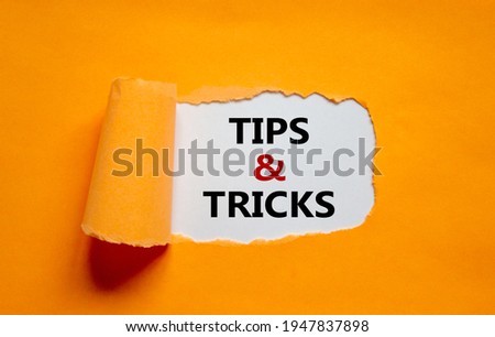 Tips and tricks symbol. Words 'Tips and tricks' appearing behind torn orange paper. Beautiful orange background. Business, Tips and tricks concept. Copy space.