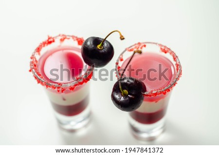 Three-layer cocktail based on vodka, cherry liqueur and syrup in drink shot glass, decorated with fresh cherry and red sugar, colorfull drink