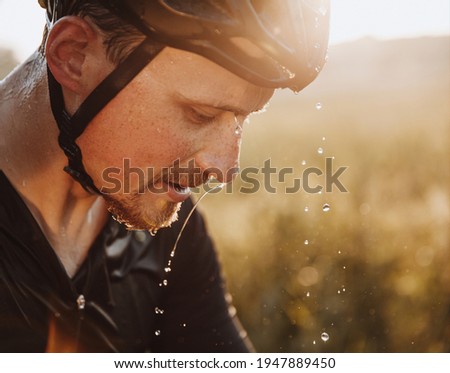 Close up portrait of tired bearded athlete in protective helmet with water drops on his face. Mature man splashed water to refresh after hard training. Royalty-Free Stock Photo #1947889450