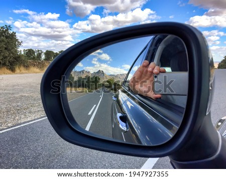 reflection in the rearview mirror of a car of a hand with a cell phone taking a picture of the reflection showing a road with a mountain landscape in the background and a hand holding a cell phone