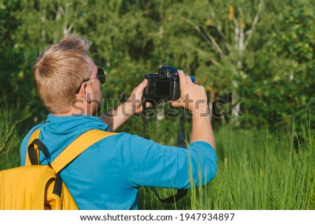 A man takes pictures with a SLR camera in the forest. Against the backdrop of beautiful greenery