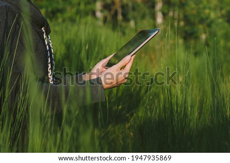 A tablet in the hands of a girl close-up. against the background of green nature
