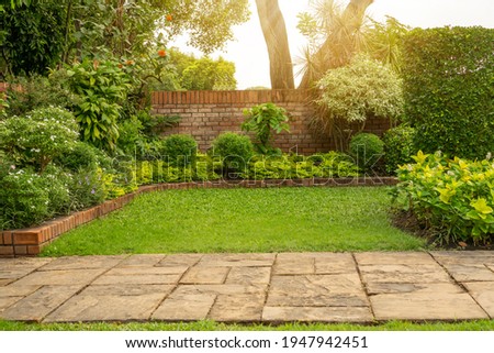 Back and front yard English cottage garden, smooth green grass lawn, colorful flowering plant and orange brick wall, evergreen trees on background, in good care maintenance landscaped in the park  Royalty-Free Stock Photo #1947942451