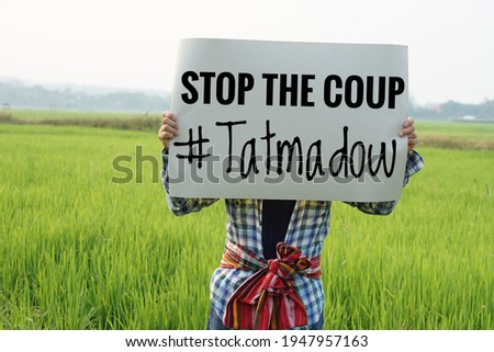 Myanmar man hold paper sign text " Stop the coup #Tatmadow". Concept protest the violence from the coup  in Myanmar. Royalty-Free Stock Photo #1947957163