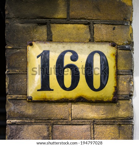 enameled house number one hundred and sixty . Black lettering on a yellowish plate.