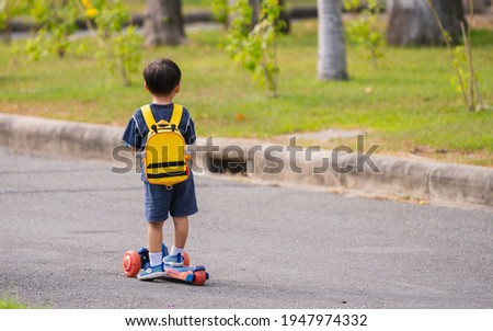 Little boy was standing on a scooter looking at something by the road.