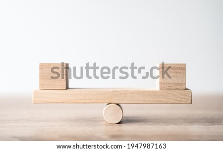 Symbol of scales. Wooden cubes figures Balancing On Wooden Seesaw. A wooden plank balancing on a wooden wheel. Concept of harmony and balance, work or family, career or relationship. Space for text Royalty-Free Stock Photo #1947987163