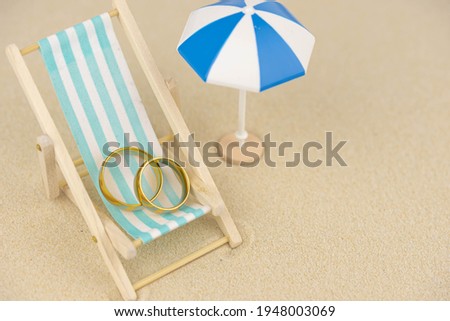 Two golden wedding rings close up on a sun lounger on sand. Wedding on the beach invitation card concept.