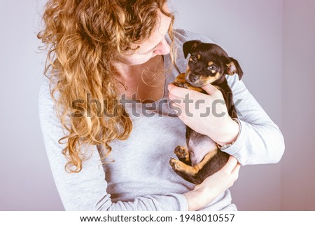 Part of a woman with brown curls, she lovingly cuddles a tiny Jack Russel Terrier puppy in her arms. In vintage, retro colors