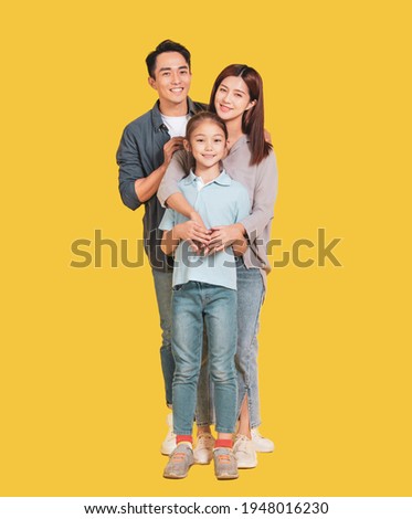 Happy Asian young family with one child standing embracing and smiling at camera isolated on yellow