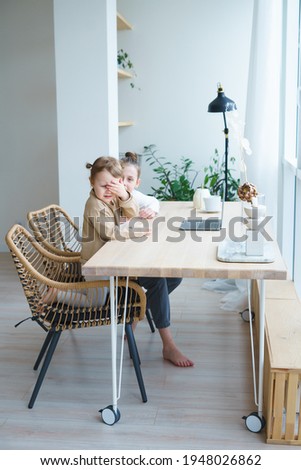 two sisters girls a child in light pajamas and a white sweater talk, watch cartoons at the table, communicate emotionally in front of a large window