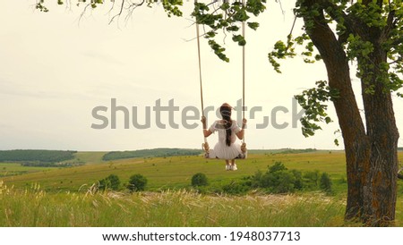 A young girl in dress swinging on swing in evening park. Wooden swing with swinging free, happy woman outdoors. Swing on a swing, dreams of flying. Travel in spring summer in nature. Healthy lifestyle Royalty-Free Stock Photo #1948037713