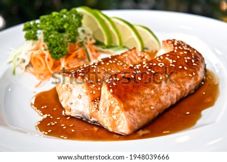 Grilled salmon teriyaki with vegetables and citrus Japanese food on white plate, on black background Royalty-Free Stock Photo #1948039666