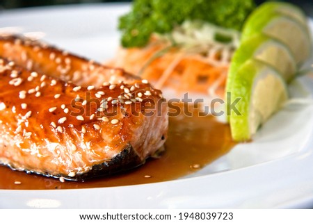 Grilled salmon teriyaki with vegetables and citrus Japanese food on white plate, on black background Royalty-Free Stock Photo #1948039723