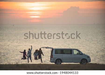 The four friends have fun near the minivan against the sunset sky Royalty-Free Stock Photo #1948044133