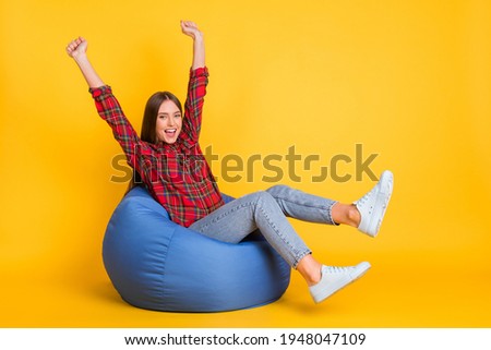 Portrait of attractive cheerful lucky girl sitting in bag chair having fun isolated over bright yellow color background
