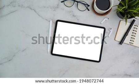Top view of modern workplace with digital tablet, stylus pen, notebook, coffee cup and wireless earphone on marble background.