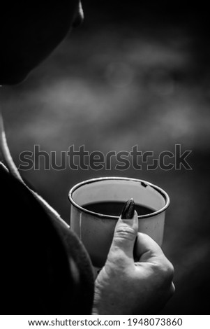 The girl is holding a white mug in the forest. Female hands hold a white mug on the background of the forest. Black and white photo. 