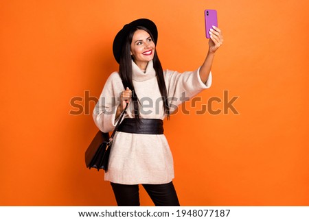 Portrait of attractive cheerful woman influencer taking making selfie posing isolated over bright orange color background