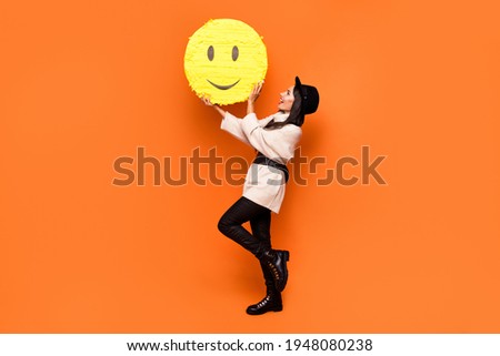 Full size photo of young beautiful charming smiling girl hold huge yellow smile emoji isolated on orange color background