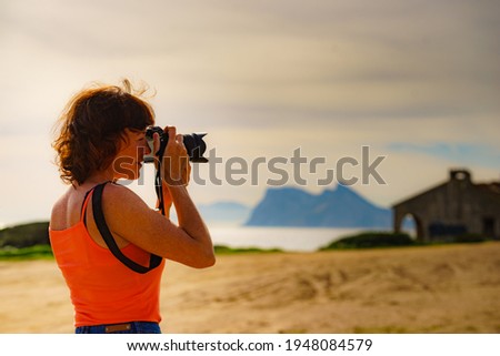 Female tourist on holidays taking photos with camera. Gibraltar rock on horizon. Torrecarbonera beach, Punta Mala, Andalusia Spain.