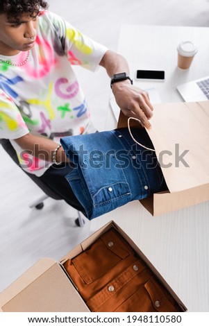 High angle view of african american owner of showroom putting shirt in shopping bag