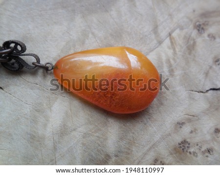 Bright yellow amber stone and dark metal chain on the background of a beautiful wooden surface.