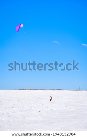 A person on a snowboard with a kite in the field