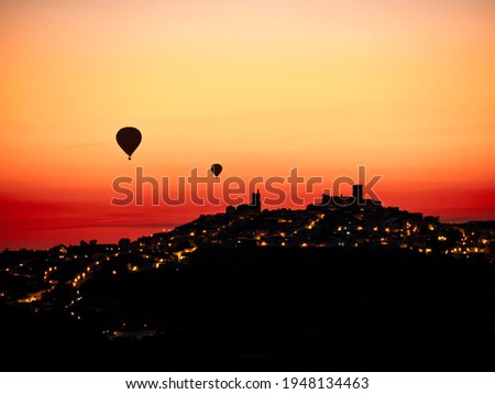 Unfocused Silhouette of balloons flying over town at sunrise.