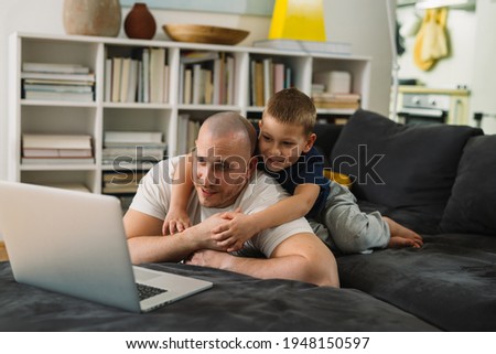 father and son using laptop computer at home. they are relaxing sofa