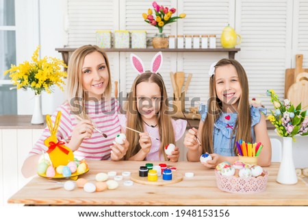 Portrait of a mother with her daughters in the kitchen. The family paints eggs. Preparing for Easter at home..