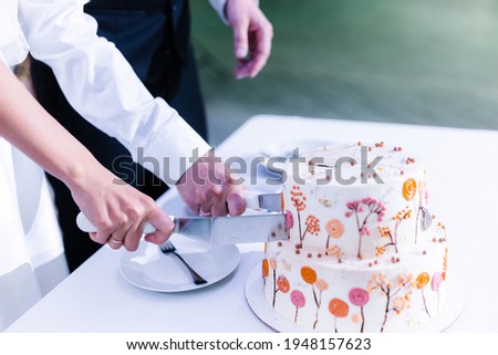 hands cut the wedding cake in two tiers with autumn pictures